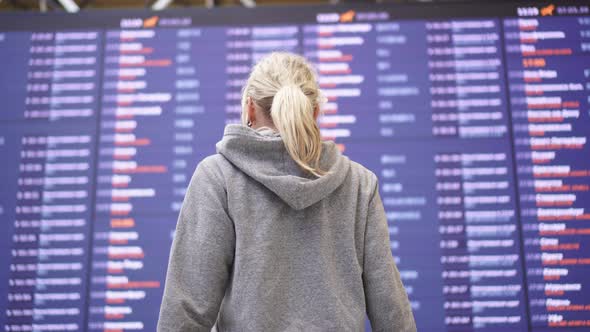 Woman Tourist on the Background of Information Board at the Airport.