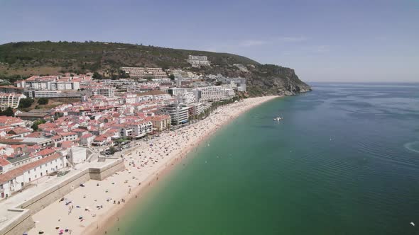 Seagulls flying above the ocean, Sesimbra sand beach and cityscape against hills. Aerial view