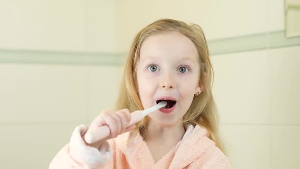 Happy Smiling Little Girl Brush Teeth Using Ultrasonic Electric Toothbrush in Bathroom at Home