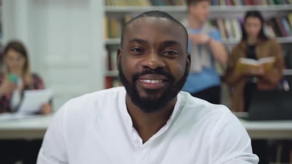 Positive Bearded Young Black-Skinned Man Looking at Camera in the Library