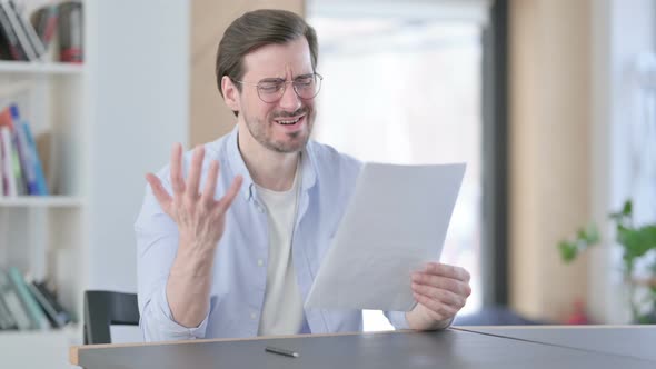 Man in Glasses Reacting to Loss While Reading Documents