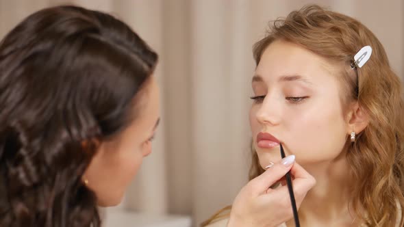 Makeup Master Puts Makeup on the Face of the Client. Applying Paint To the Lips of the Girl