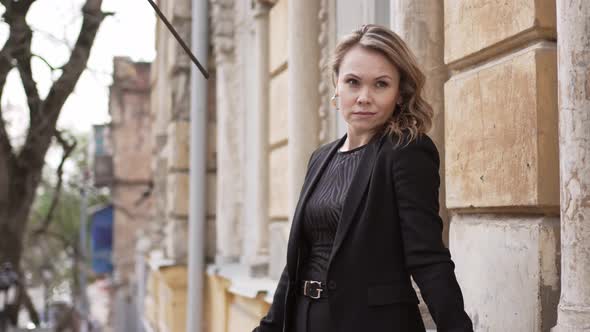 an Attractive and Calm Woman in a Black Suit on the Balcony of an Old Building