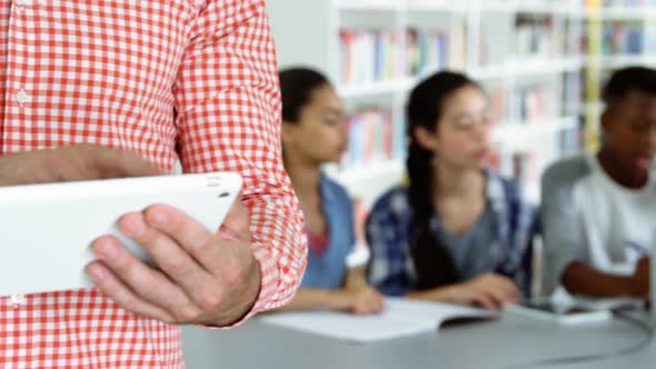 Teacher using digital tablet while student studying in background