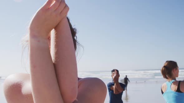 Caucasian woman doing yoga on the beach with group of women and blue sky background