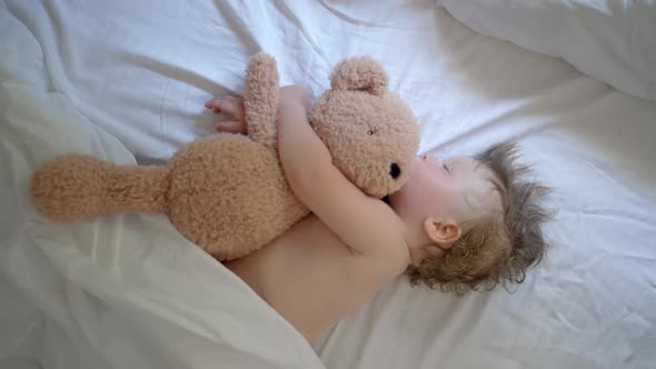 Sleeping Baby Happy and Carefree in Bed Hugging a Teddy Bear Toy