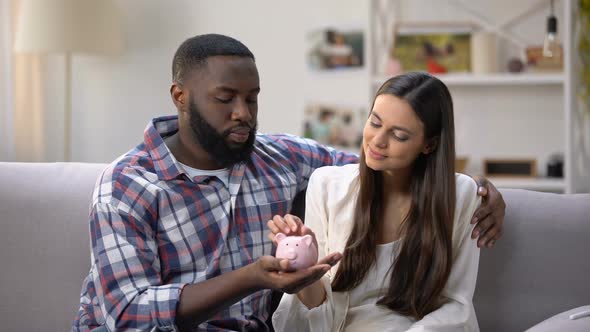 Mixed-Race Couple Putting Coins in Piggy Bank, Social Program for Young Families