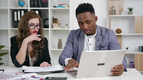 Woman and Black-Skinned Businessman Working Together in Modern Office with Laptop and Documents