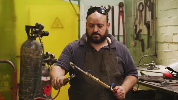 Caucasian male factory worker at a factory standing in a workshop, holding an ignited welding gun