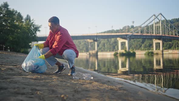 African American Man Gathers Rubbish Cleaning River Beach