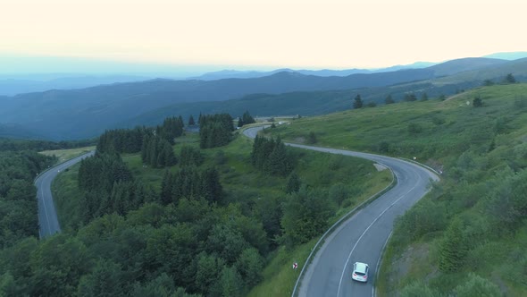 Drone Follwoing Two Cars on Curvy Mountain Pass Road with Green Valley Below