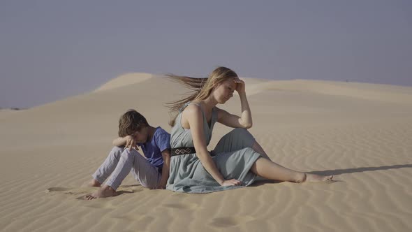 Sad Mother and Son are Sitting on a Dune in a Desert