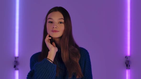 Portrait of Fashionable Model Posing in Dark Studio Against Backdrop of Bright Neon Lights