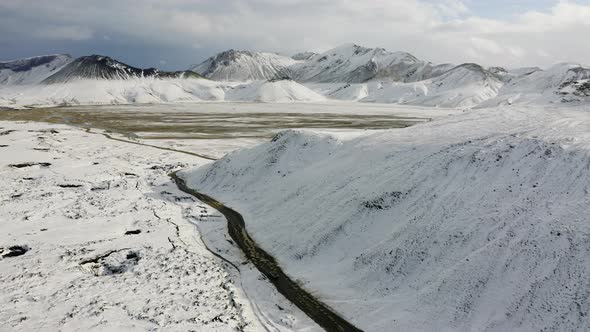 Aerial of Car Driving on Dirt Road Along the Snow Covered Mountains in Iceland