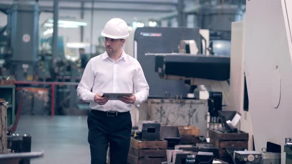 Shot of Professional Factory Worker Wearing Hard Hat Holds Tablet Computer Walking Thorugh Modern