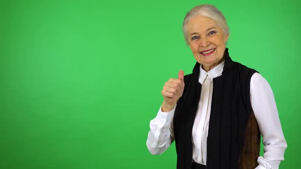 An elderly woman smiles and shows a thumb up to the camera - green screen studio