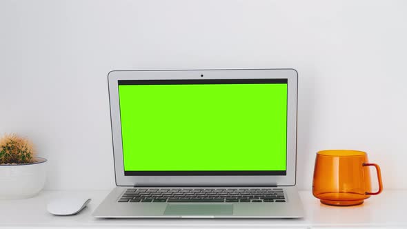 Laptop with mockup green screen on a white table with house plant and tea in home office. Stop motio