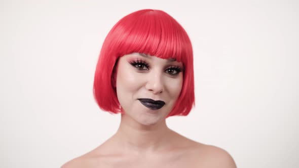 Portrait of Caucasian joyful stylish woman in pink wig smiling to camera on light background