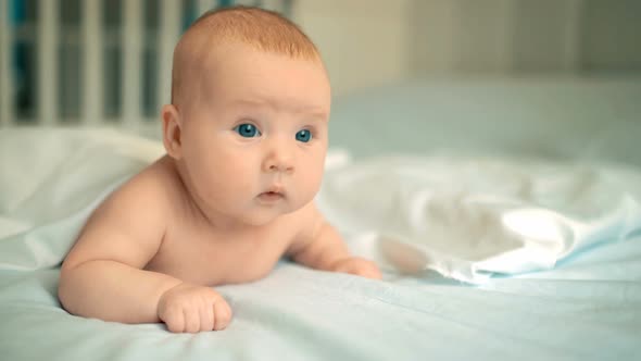 Cute Baby with Beautiful Blue Eyes Lying in White Bed