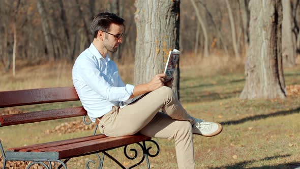 Businessman Relaxing And Reading Fresh Newspaper. Man Sitting On Bench And Reading Newspaper.