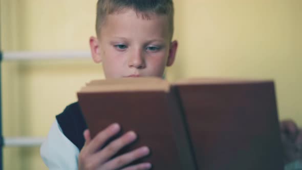 Schoolboy in Vest Does Home Task with Book in Room at Home