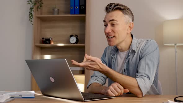 Handsome guy in a formal shirt sitting at the table and speaking on video communication