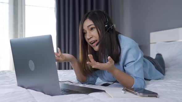 stressed business woman wear headset video conference calling on laptop computer on a bed