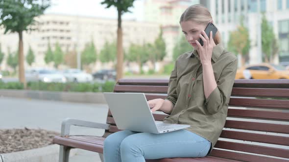 Woman Talking on Phone and using Laptop while Sitting Outdoor on Bench