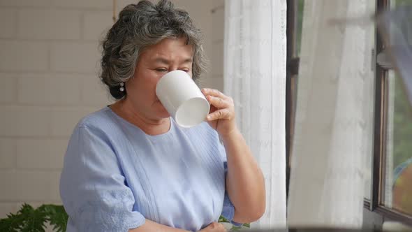 Portrait senior Asian woman drinking tea morning beside a window at home.