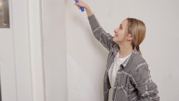 Closeup of a Young Woman Paints a White Wall with a Roller in the Apartment