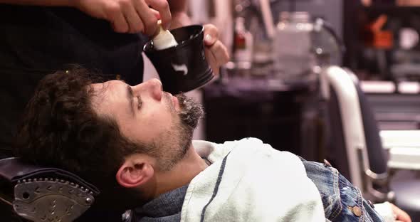 Man getting his beard shaved with shaving brush in barber shop