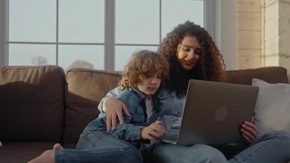 Boy Sits with His Mom on a Couch Looking at the Laptop at Home on a Sunny Day