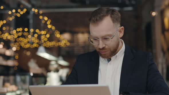 Businessman Sitting at the Cafe and Typing Something at Laptop