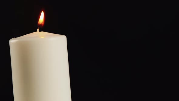 A Burning White Candle on a Black Background or in the Dark