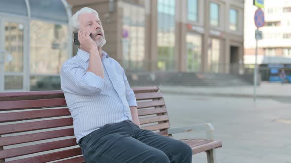 Old Man Talking on Phone While Sitting Outdoor on Bench
