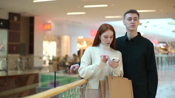 Portrait of Puzzled Young Couple Looking for Store in Shopping Mall Centre Browsing App on Mobile