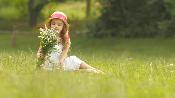 Child Holds a Bouquet of Wildflowers in Her Hands, She Smells Them and Smiles. Slow Motion