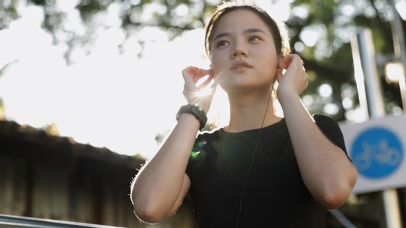 Asian woman jogging exercising running listening to music in the autumn forest on a warm sunny day.