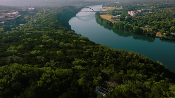 Aerial tilt up over Lake Austin greenbelt to reveal Pennybacker 360 bridge during hazy summer sunris