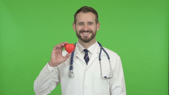 Young Male Doctor Holding a Heart Shape and Smiling Against Chroma Key