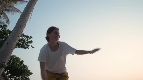 The Girl Goes on a Slackline at Sunset on a Tropical Beach