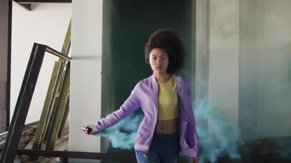 Mixed race woman holding green flare walking through an empty building