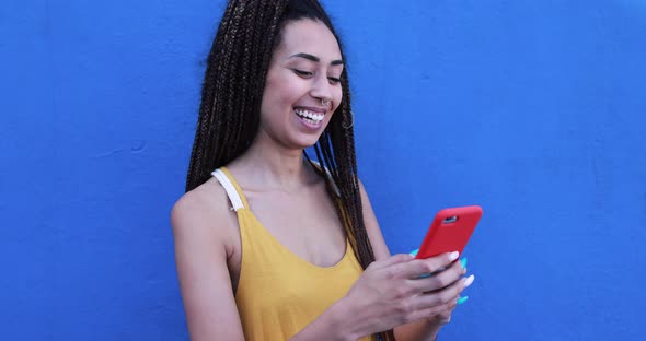 Bohemian mixed race young woman using smartphone outdoor with blue background