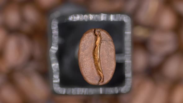 Top View Of A Roasted Arabica Coffee Bean Rotating Against Blurry Coffee Beans Backdrop. close up