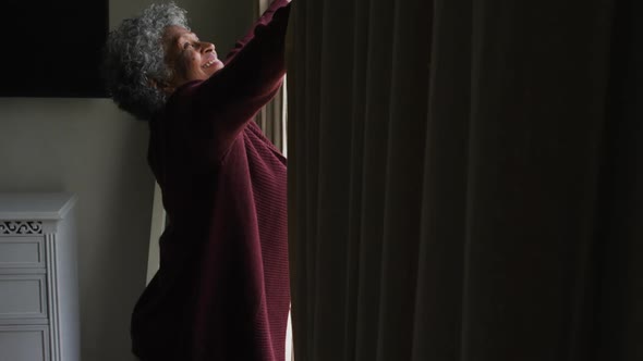 Senior african american woman opening curtains of the window at home