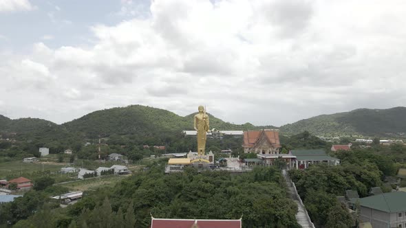 Drone Flying backwards from Golden standing Buddah Statue at Wat Khao Noi temple, Hua Hin. Thailand