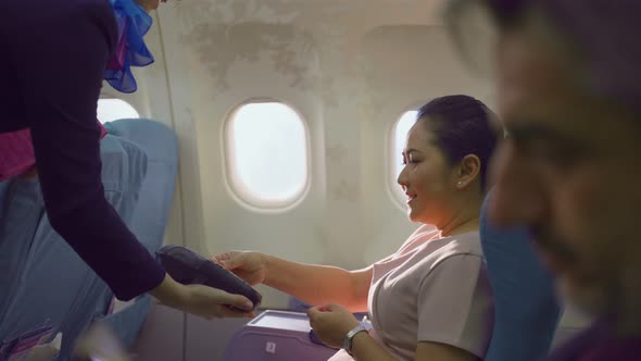 Asian senior woman buying gift from air hostess and paying by credit card tap on machine in airplane