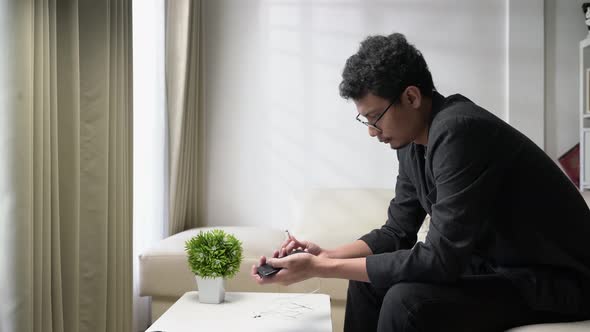 Asian young man with glasses wearing or pair earphone to his smartphone to listening music