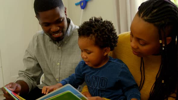 Front view of young black parents and son reading a story book and sitting on floor at home 4k