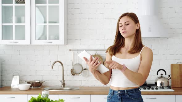 The girl in the white kitchen holds a tablet in her hands and considers the diet.